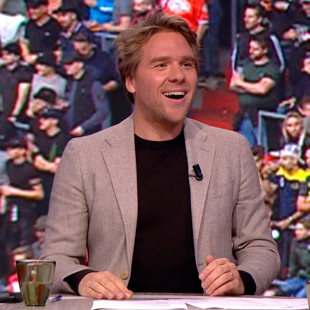 Close-up foto van Sjoerd aan tafel tijdens Studio Voetbal, met lichtbruin colbert